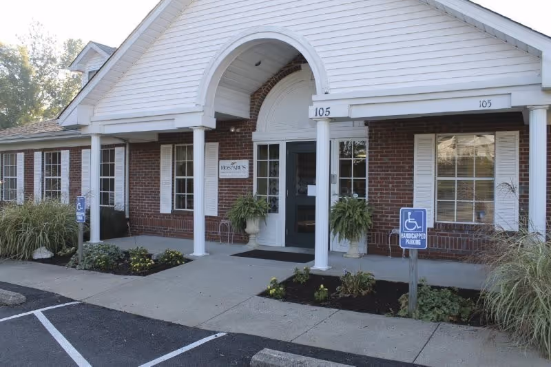 Brick facility entrance with white columns, curved arch, and accessible parking signs.