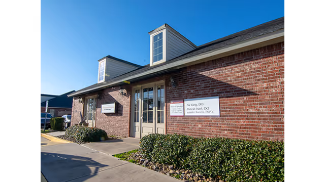 Brick facility exterior shows the main entrance, signage, and landscaped shrubs.