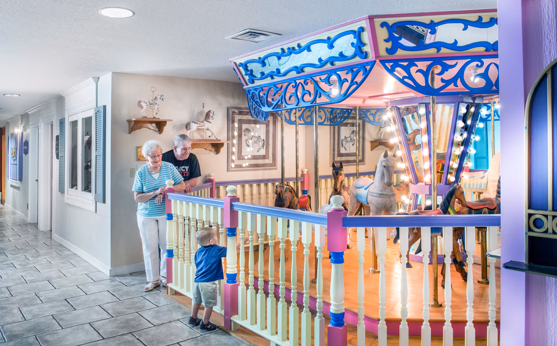 Colorful carousel ride inside a senior living hallway, with elderly residents and a child nearby.