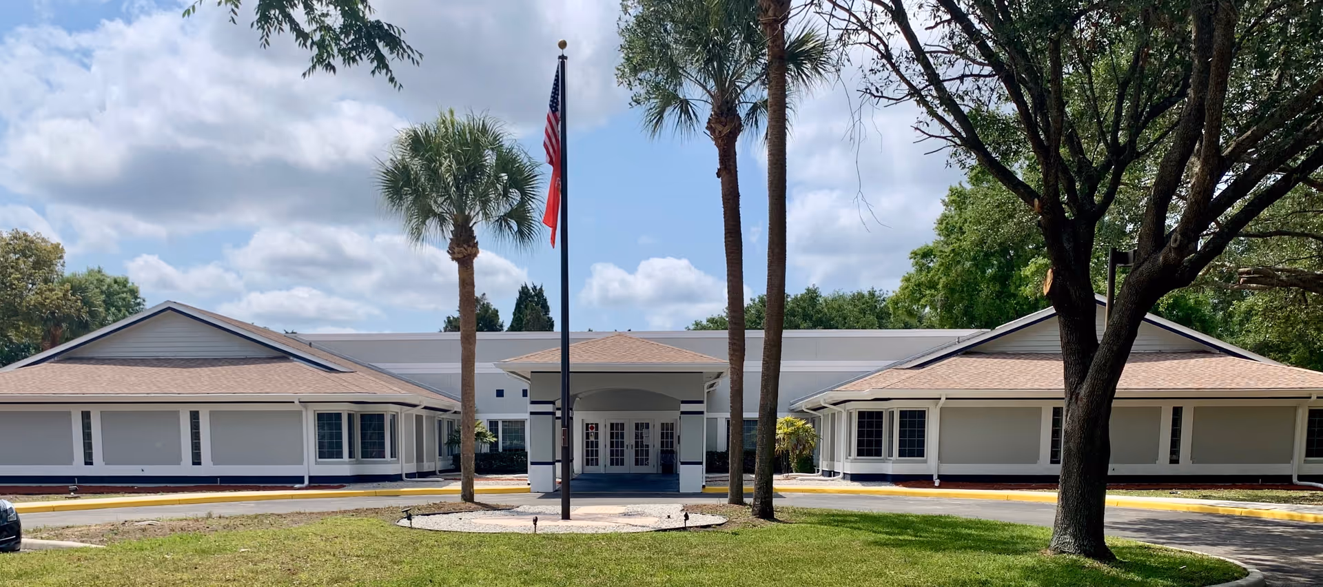 Exterior view of Atrium Gardens Assisted Living building with flagpole and palm trees