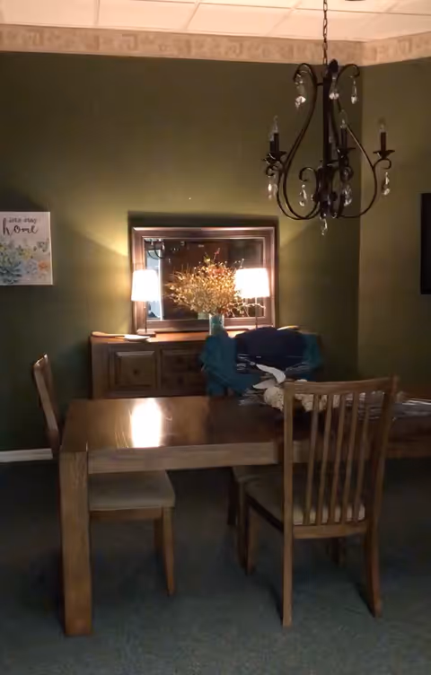 A wooden dining table and chairs in a dimly lit dining room with a chandelier.
