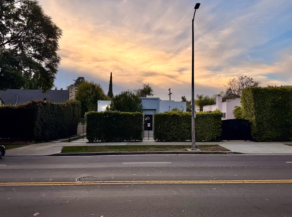 Front exterior view of a gated care facility behind trimmed hedges along the street.