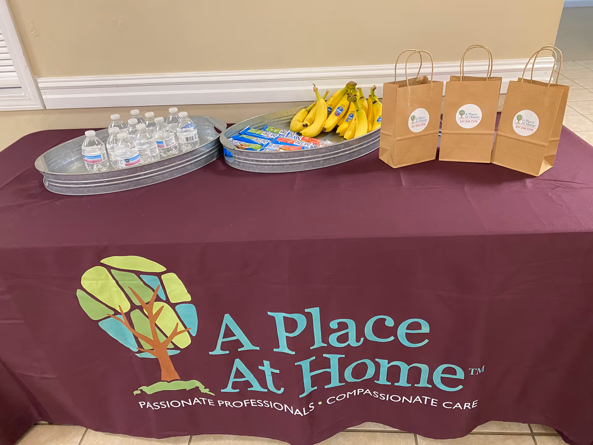 Table with water bottles, bananas, snacks, and gift bags for A Place At Home Lafayette.