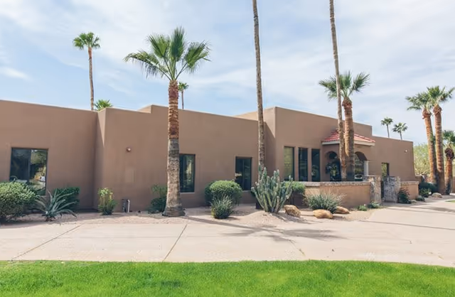 Front view of a single-story brown stucco senior living building with palm trees.