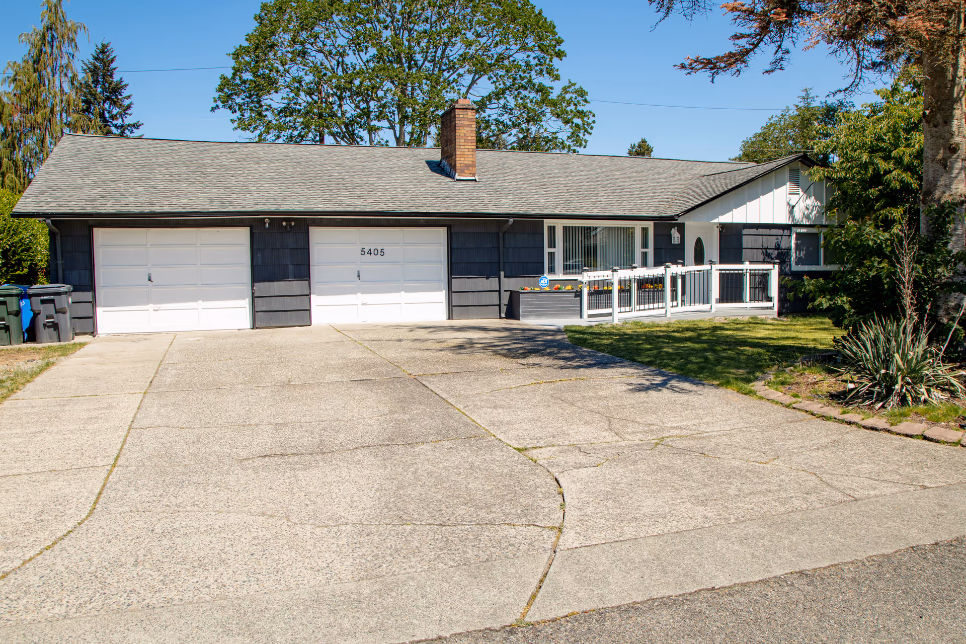 Single-story house with gray siding, white garage doors, and a paved front driveway.