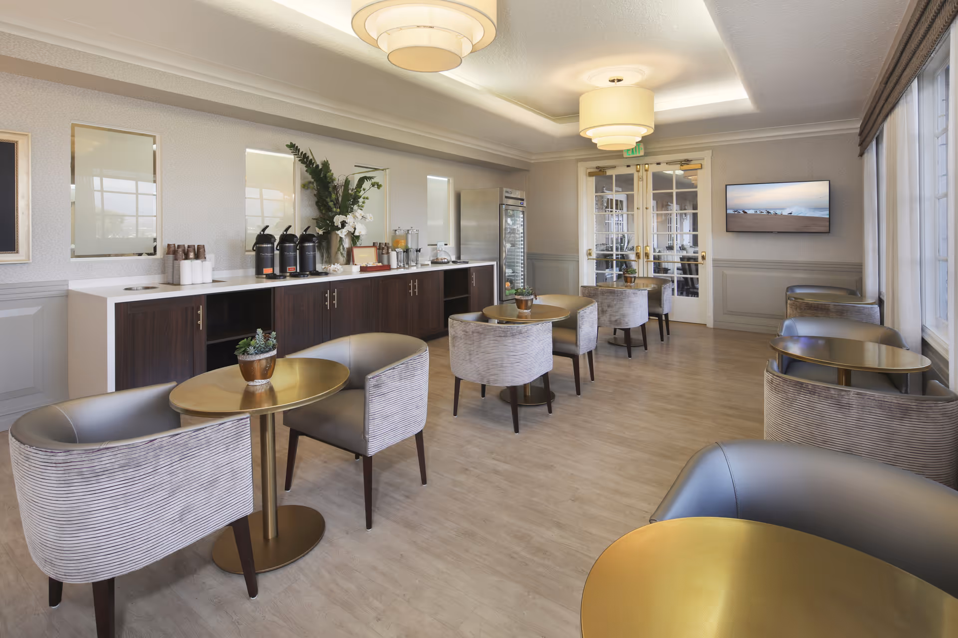Interior lounge/dining area with round gold tables, upholstered chairs, and a beverage station.