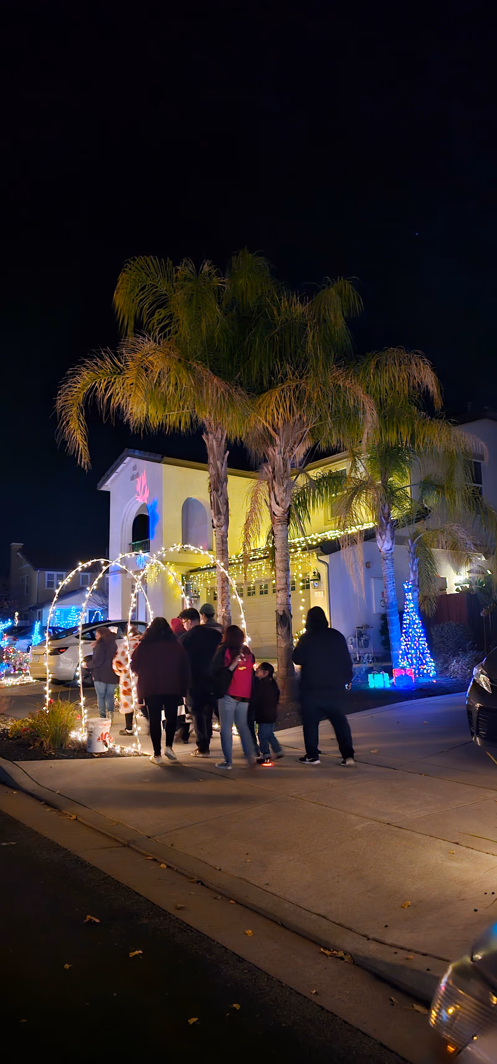 Night exterior of Angel Care Services facility with palm trees, holiday lights, and people gathered outside.