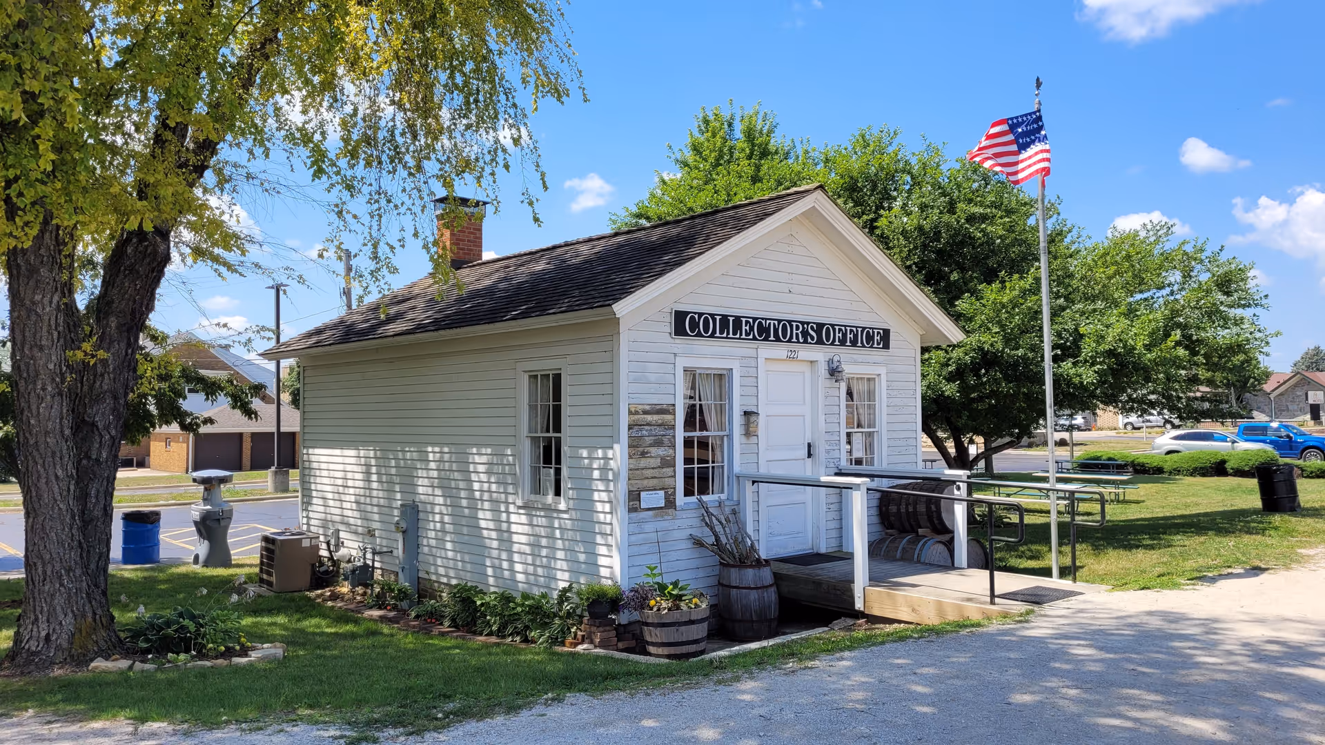 A small white wooden building labeled Collector's Office sits beside a lawn with an American flag.