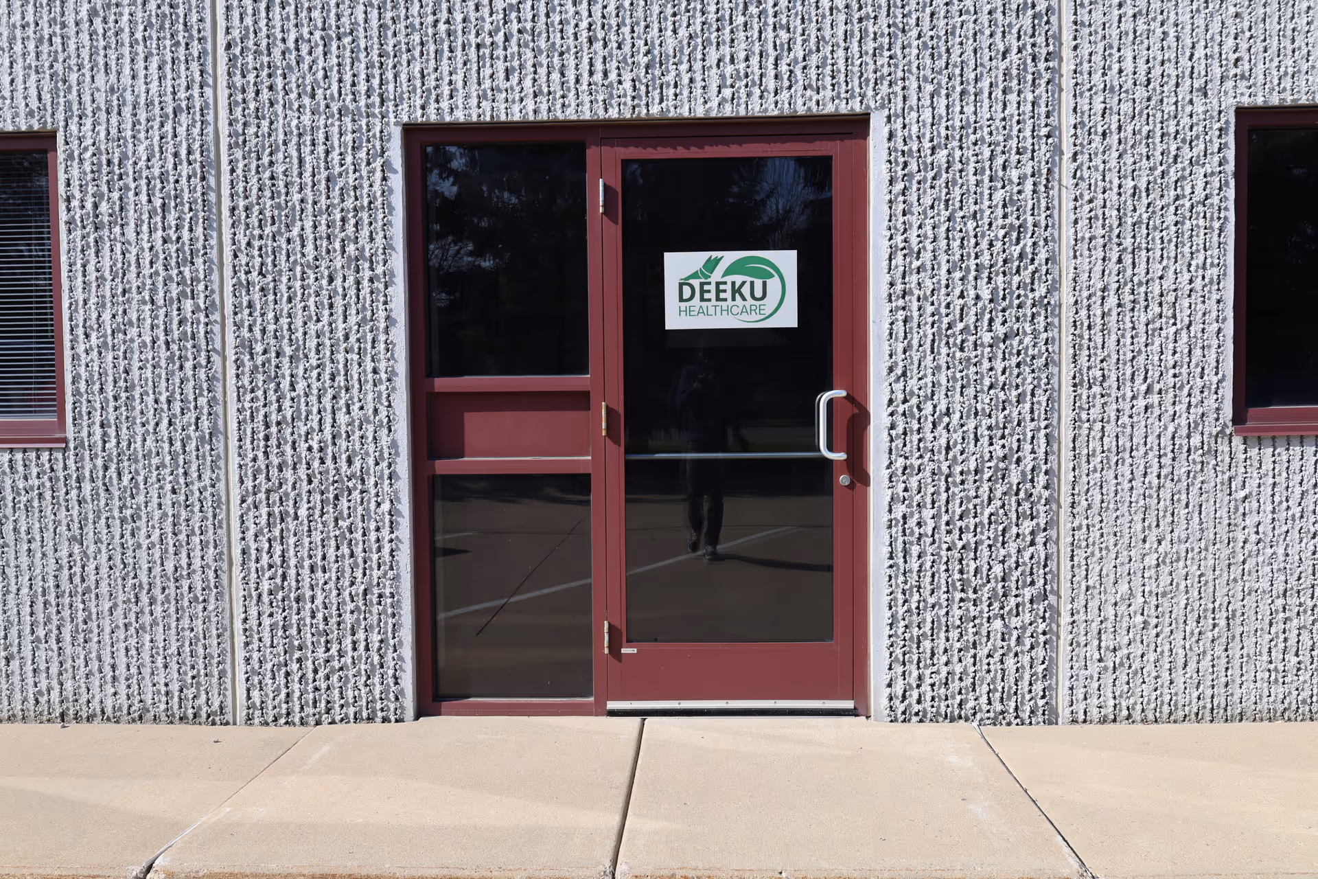 Front entrance of a Deeku Healthcare building with a burgundy door and textured exterior.