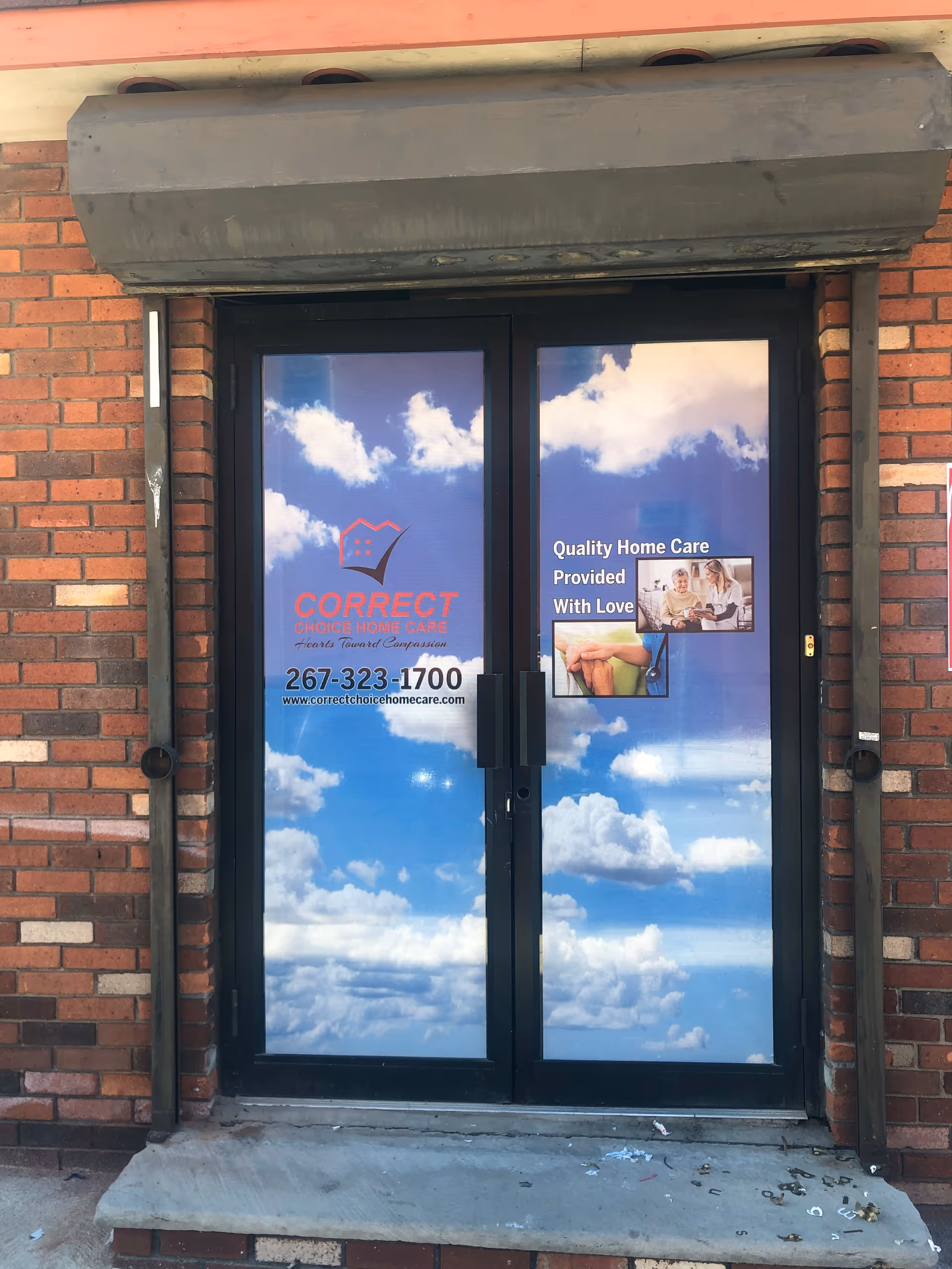 Brick exterior with glass double doors reflecting sky and Correct Choice Home Care signage.