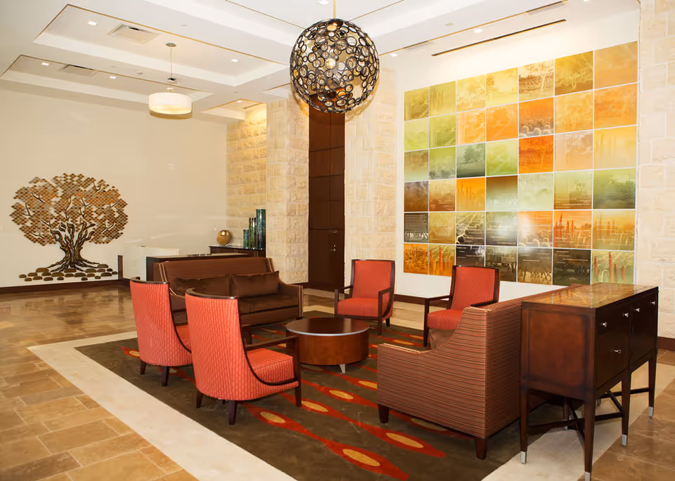 Modern senior living lobby with red chairs, brown sofa, colorful wall art, spherical chandelier.