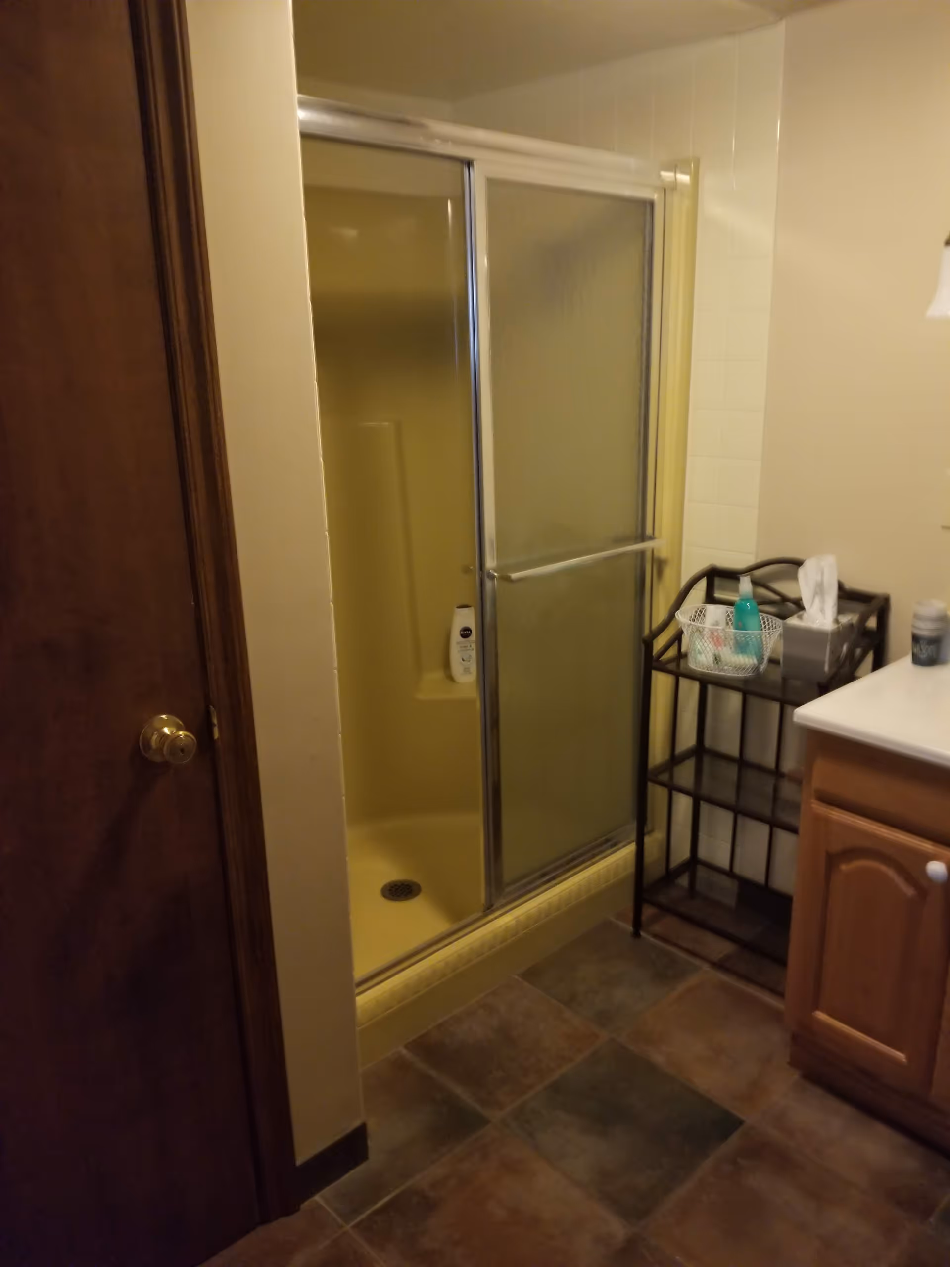 Small bathroom with sliding glass shower, tiled floor, and a wooden vanity.