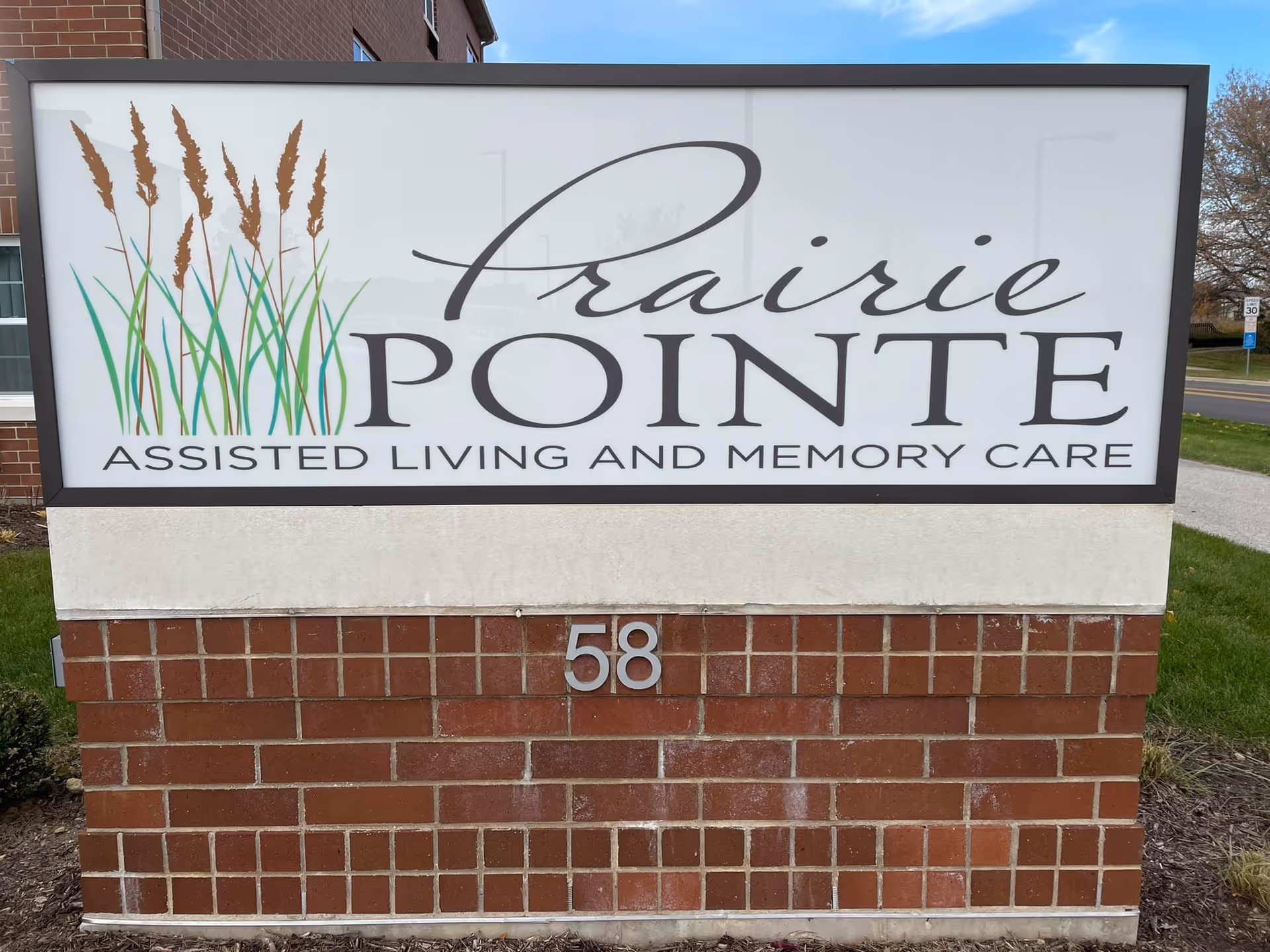Outdoor sign reading "Prairie Pointe Assisted Living and Memory Care" mounted on a brick base with the number 58.