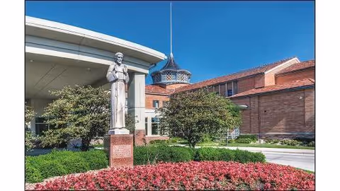 Statue near the entrance of New Cassel Retirement Center with brick building and manicured landscaping.