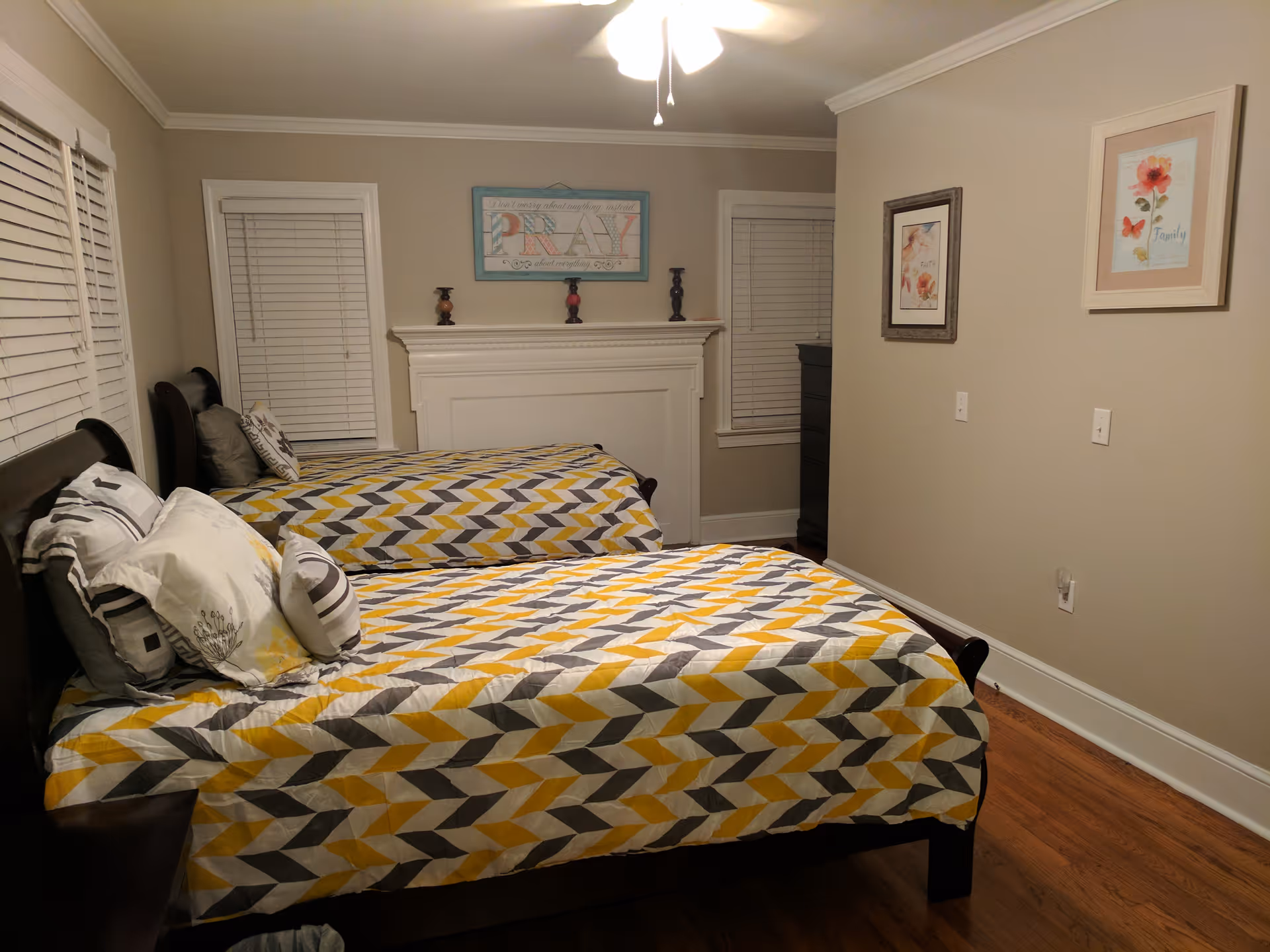 Two twin beds with geometric yellow and gray quilts flank a fireplace in a cozy bedroom.