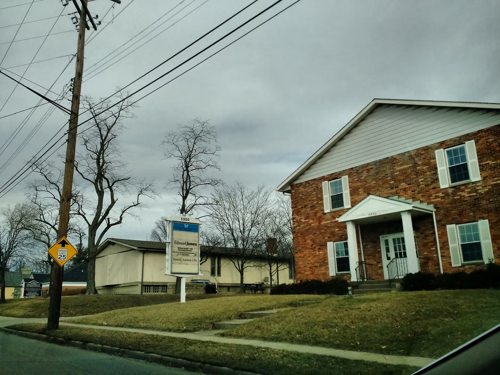 Brick building with white front porch entrance, grassy lawn, and overhead power lines.