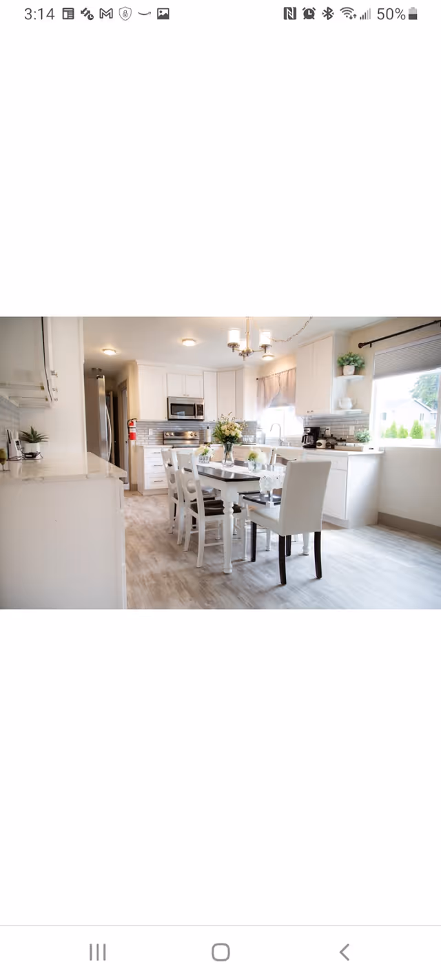 Bright white kitchen with a dining table, white chairs, plants, and stainless appliances.