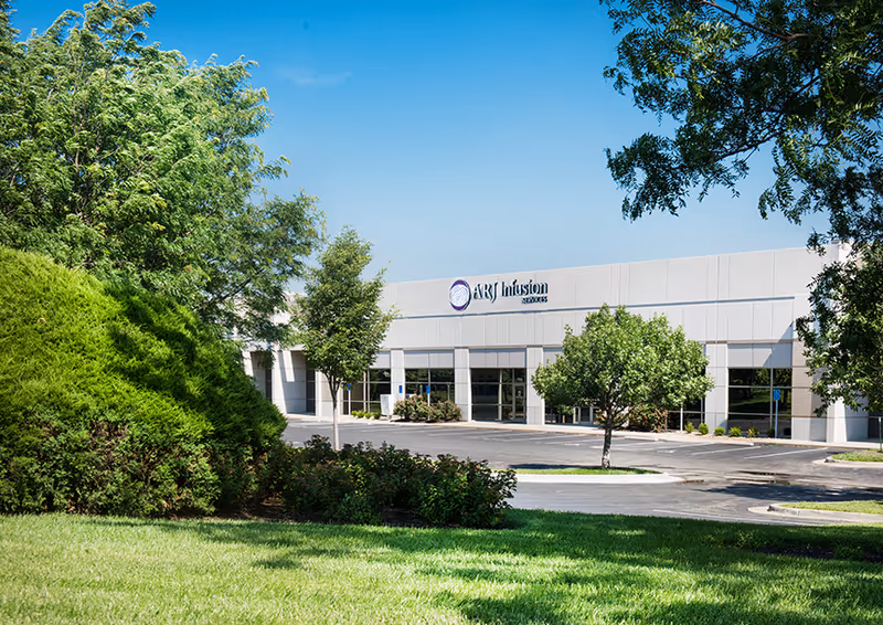 Front view of a light-colored commercial building with signage, trees, and a parking lot.