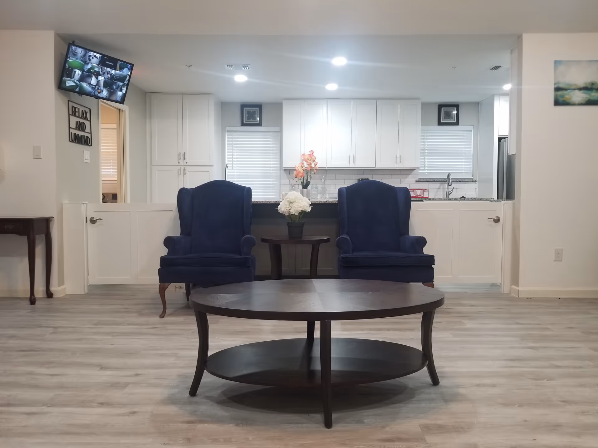 Two blue armchairs and a round coffee table in a living room area facing an open kitchen.