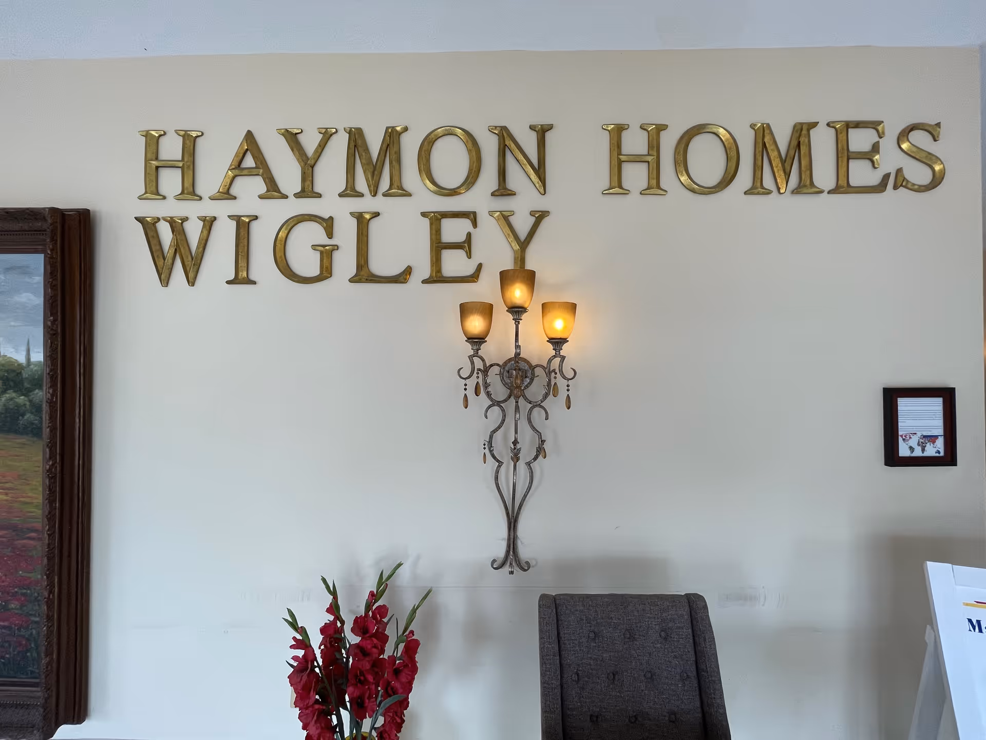 Interior lobby with gold-lettered Haymon Homes Wigley sign, ornate chandelier, and chair.