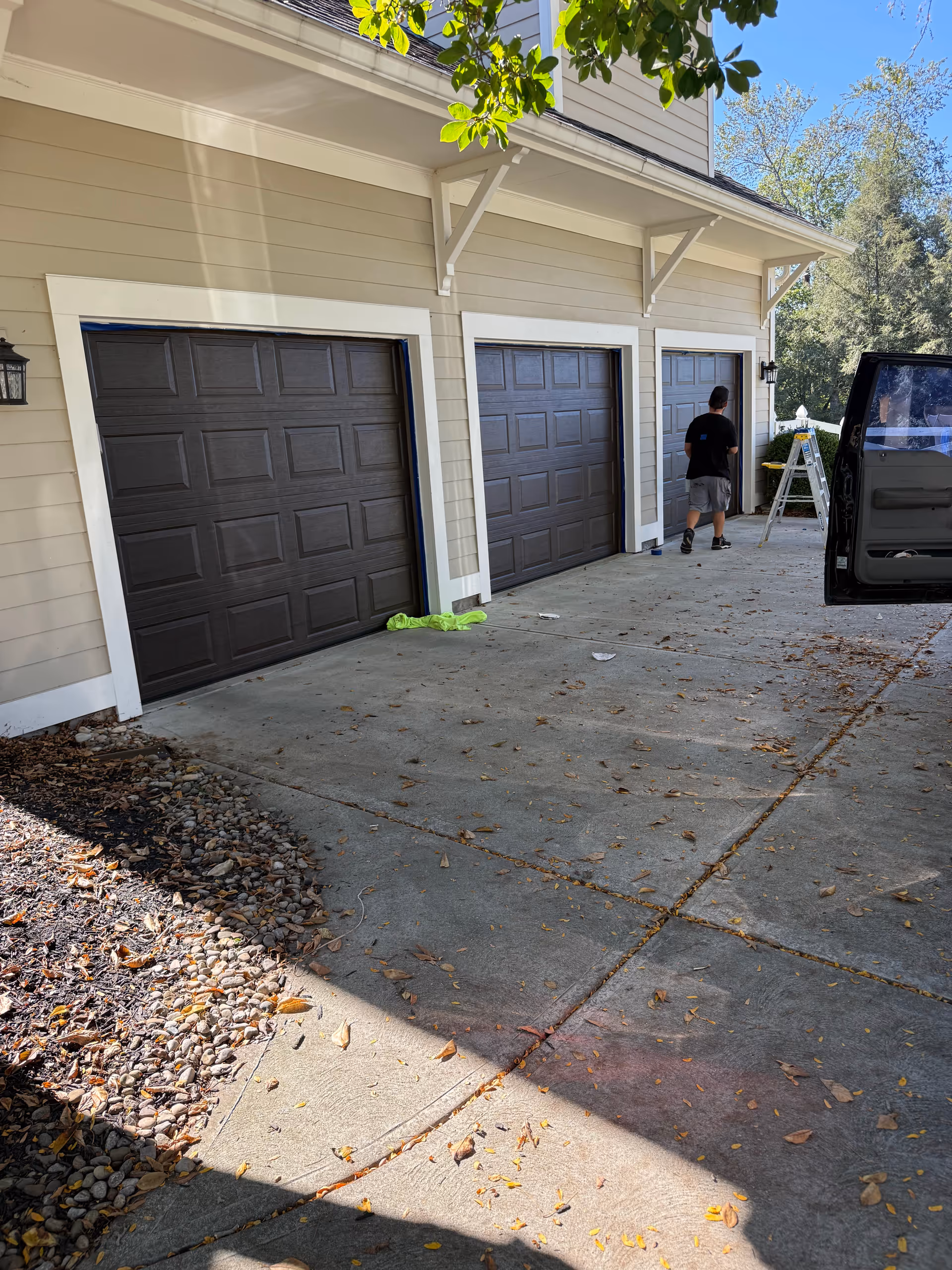 Exterior view of a facility with three garage doors and a person near a ladder.