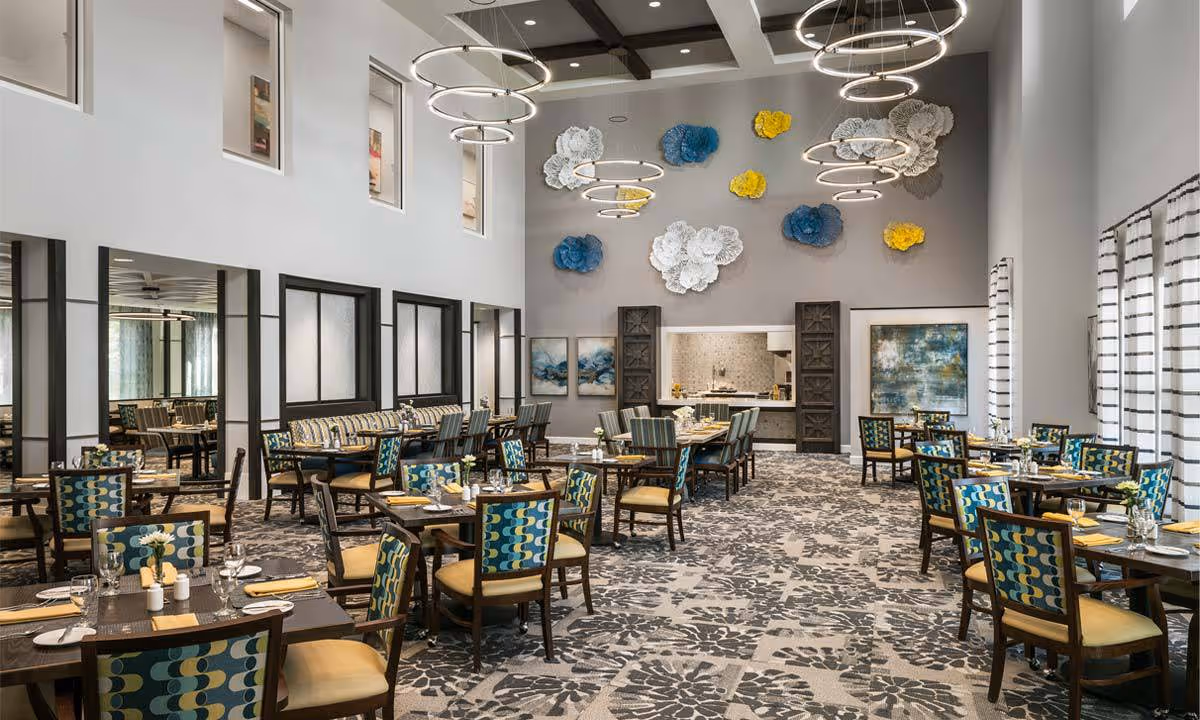 Spacious, modern dining room with high ceilings, circular light fixtures, patterned carpet, and multiple set dining tables and chairs.