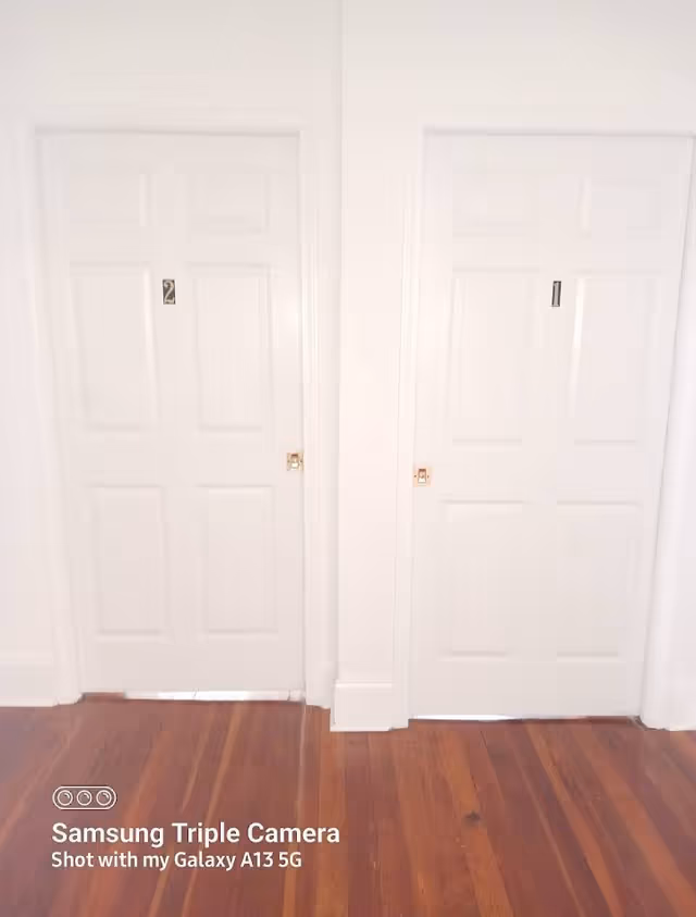 Two white interior doors along a hallway with wooden floorboards.