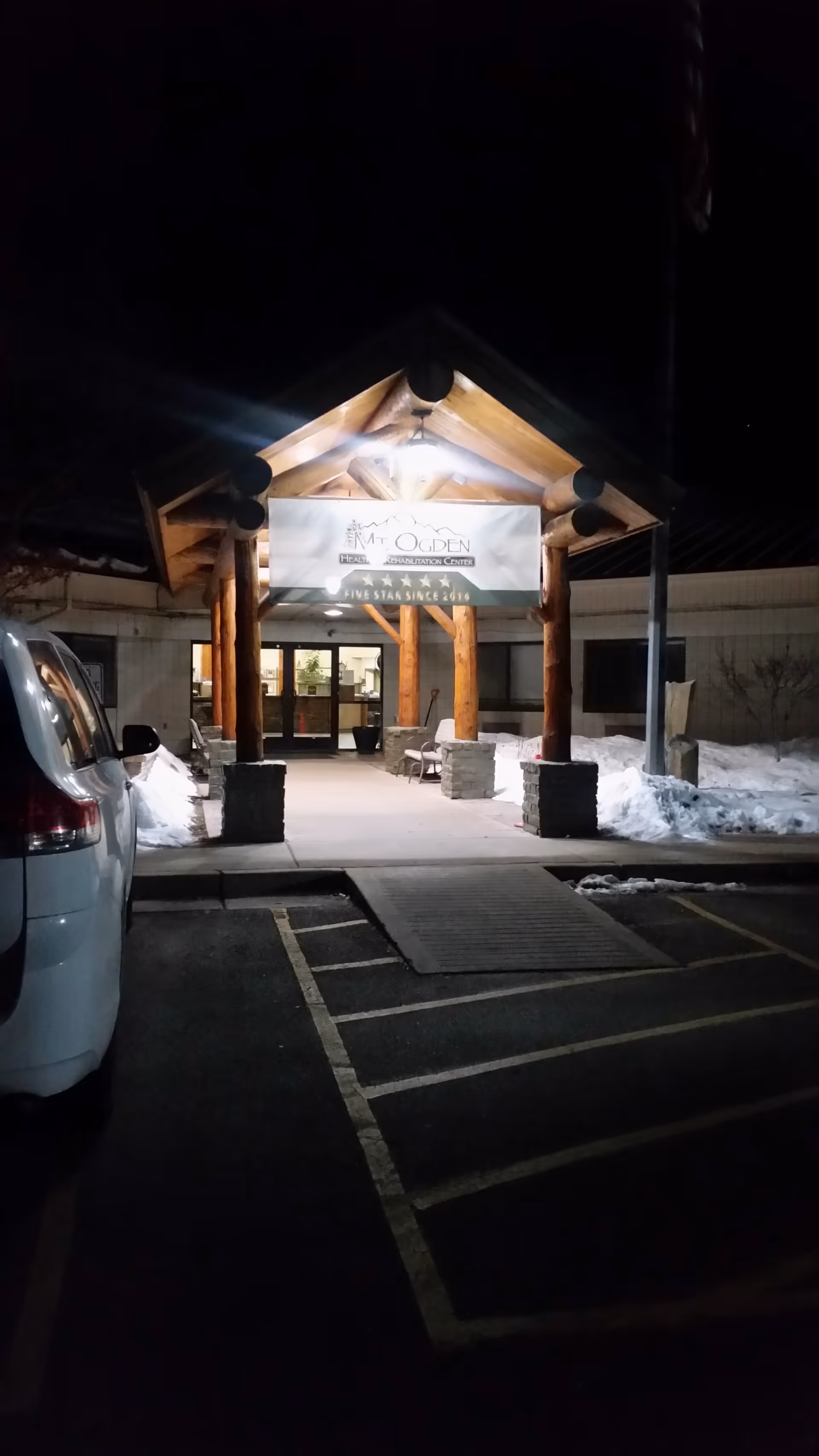 Night exterior view of Mt. Ogden Health and Rehabilitation Center entrance with wooden canopy.