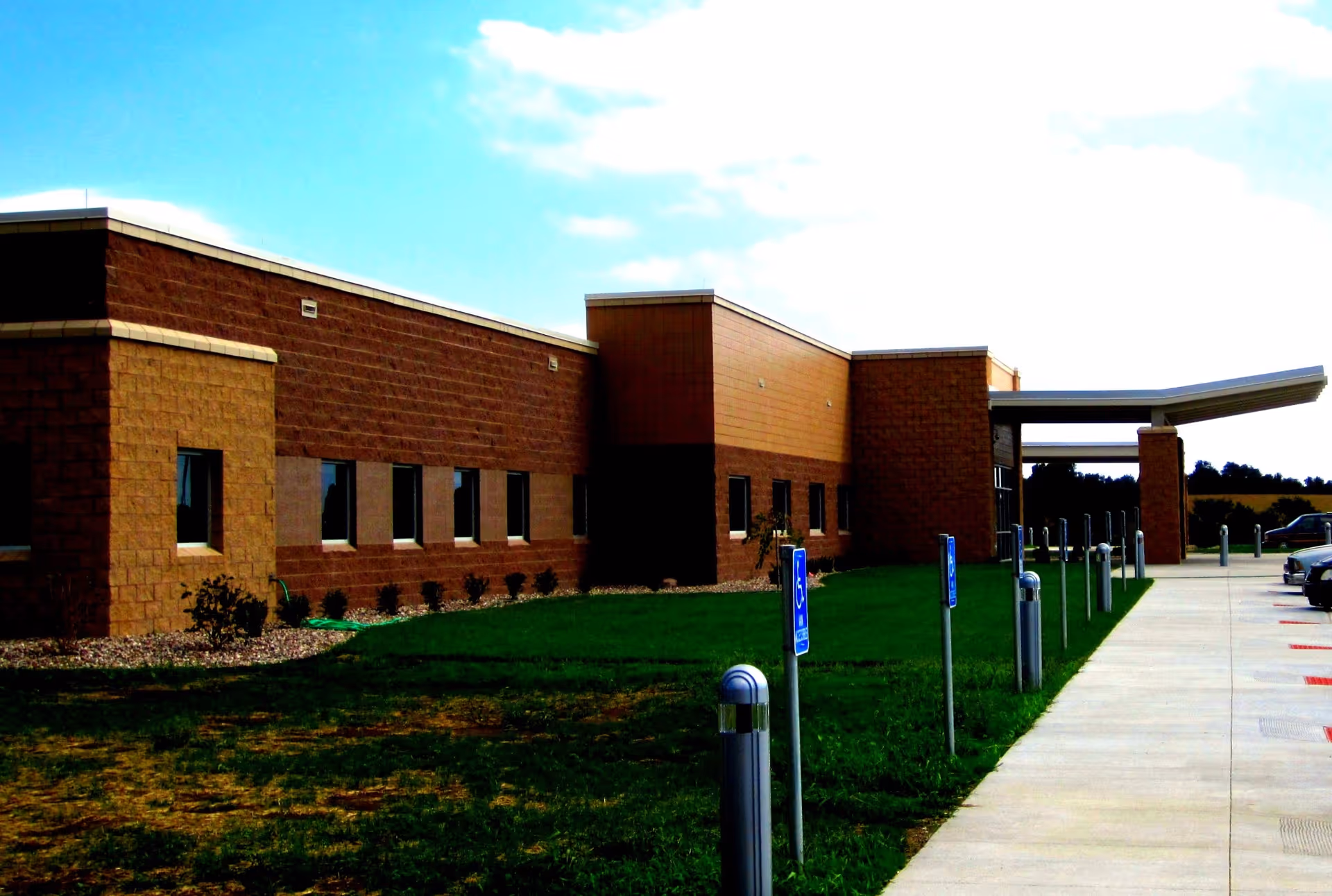 Exterior brick building with a covered entrance, parking lot, and grassy landscaping.