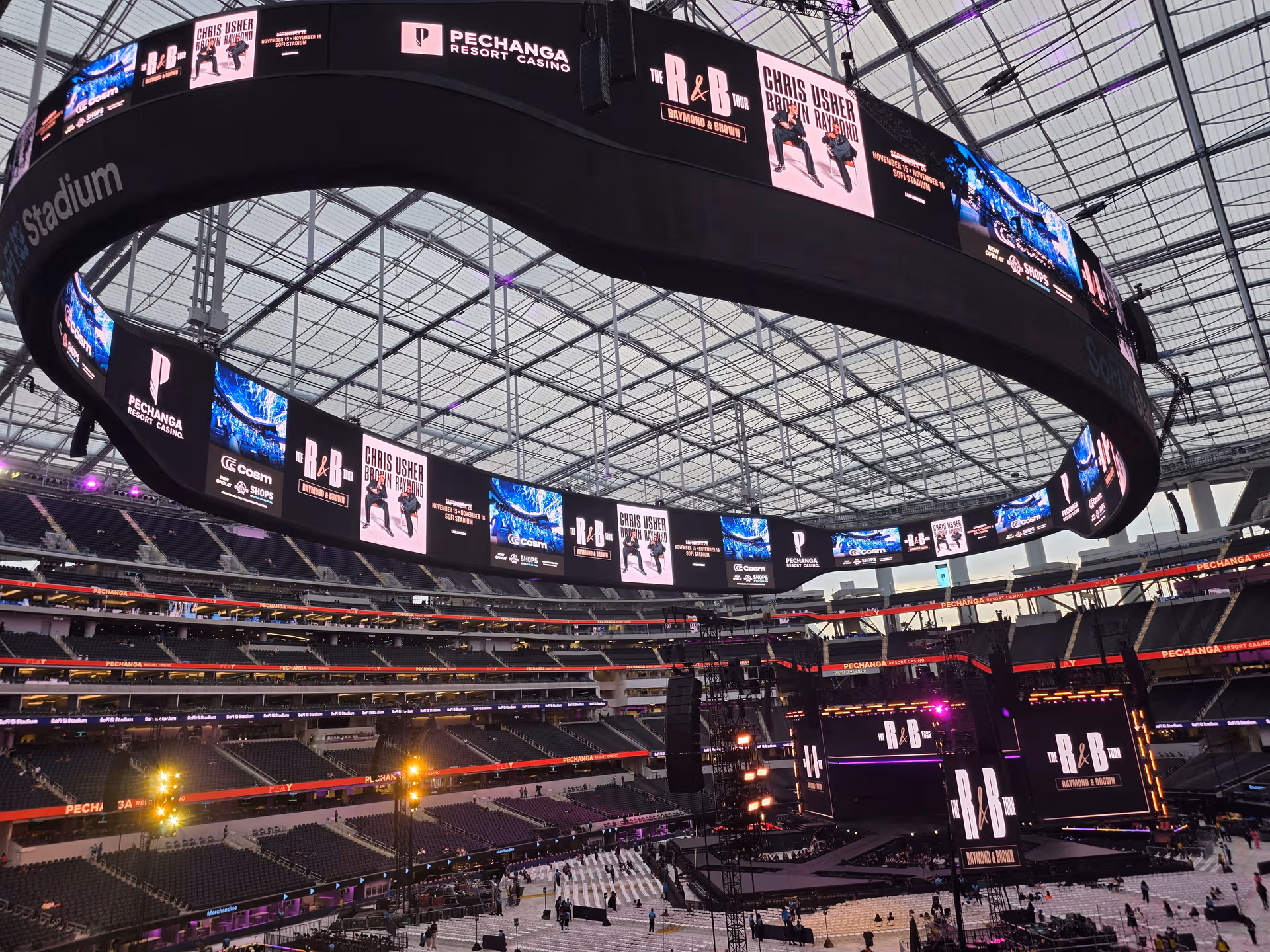 Inside a large stadium with a circular overhead video ring and stage.