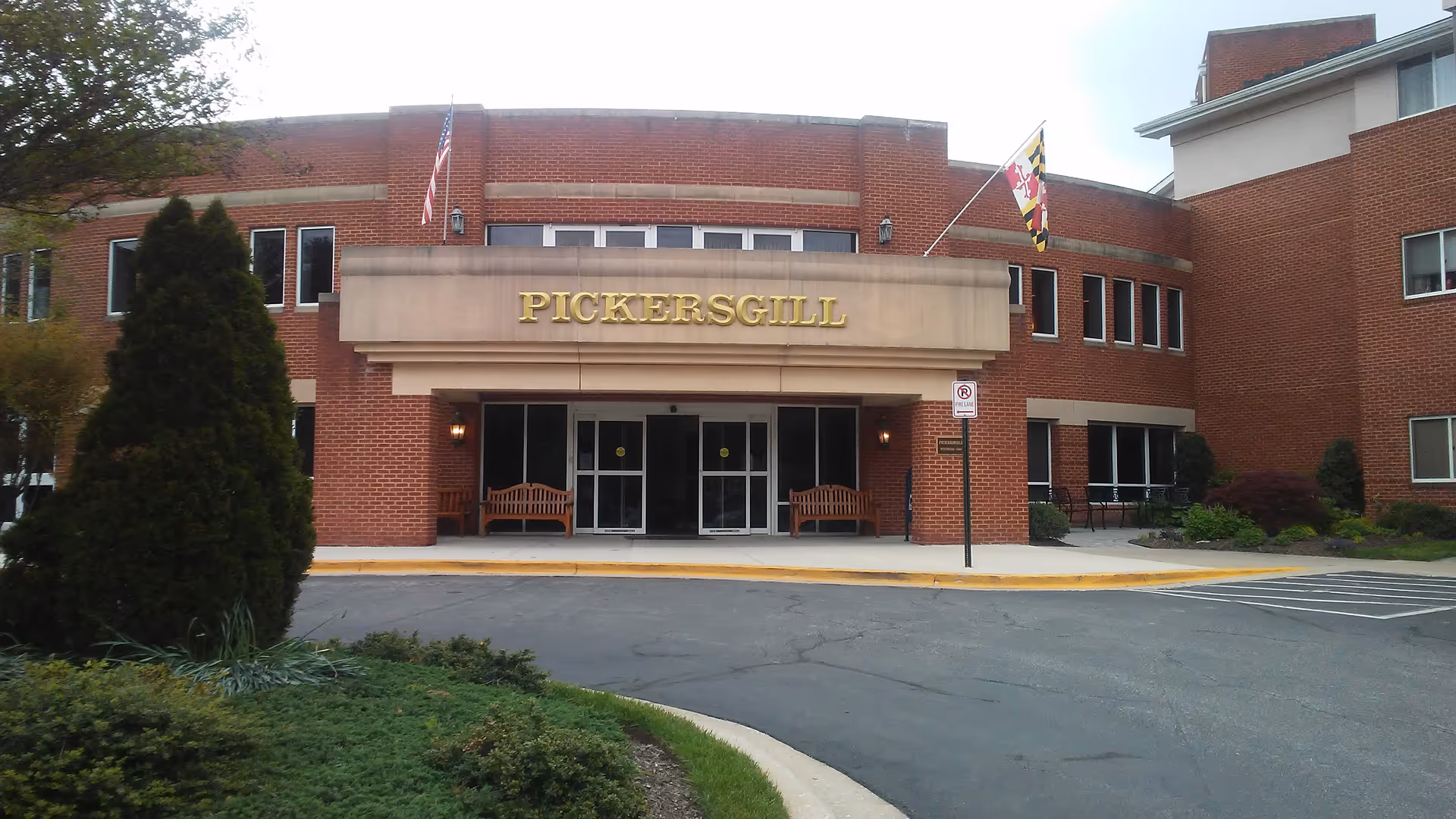 Brick retirement community building with front entrance, flags, and benches.