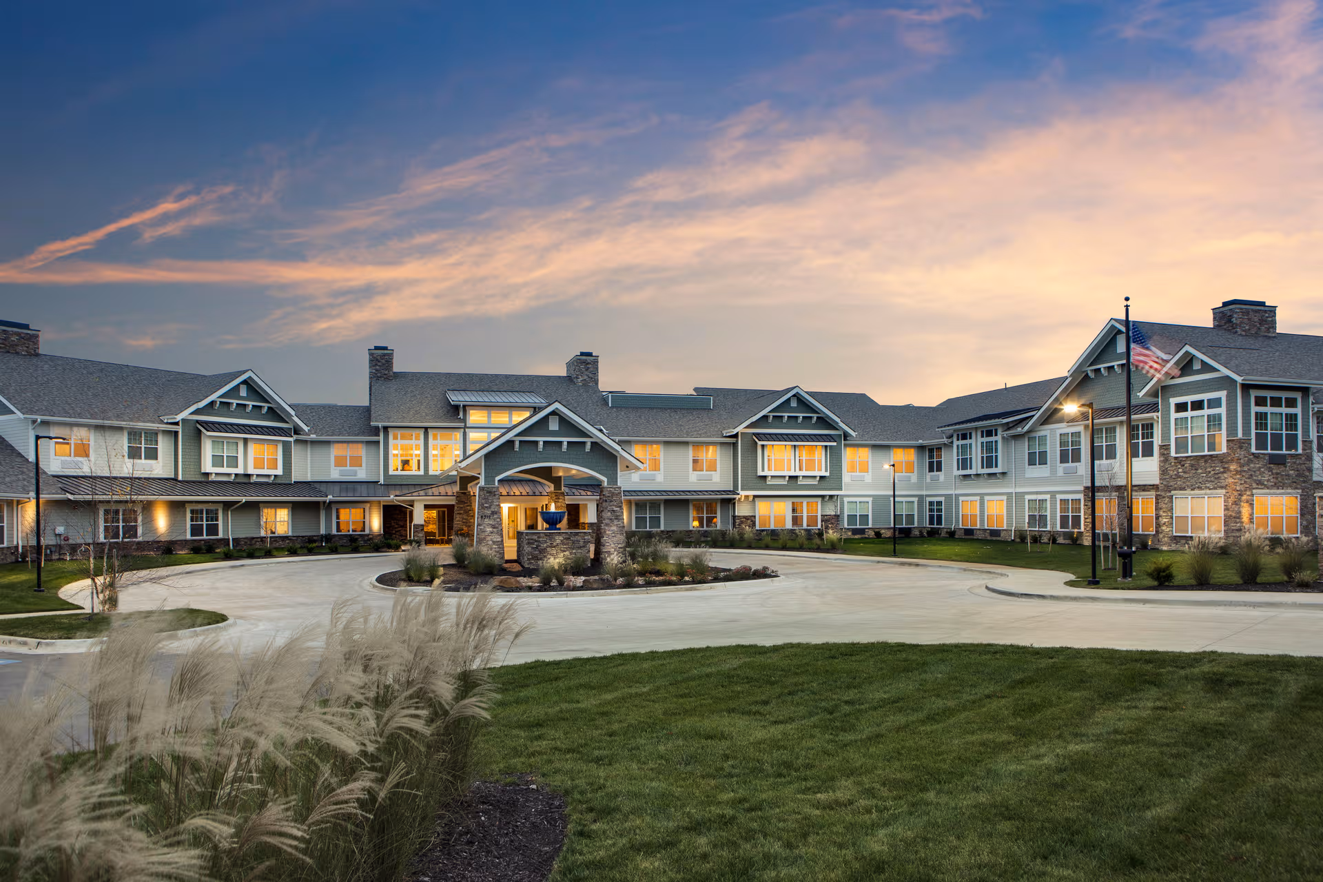 Exterior view of a senior living facility with a curved driveway and lit windows at dusk.
