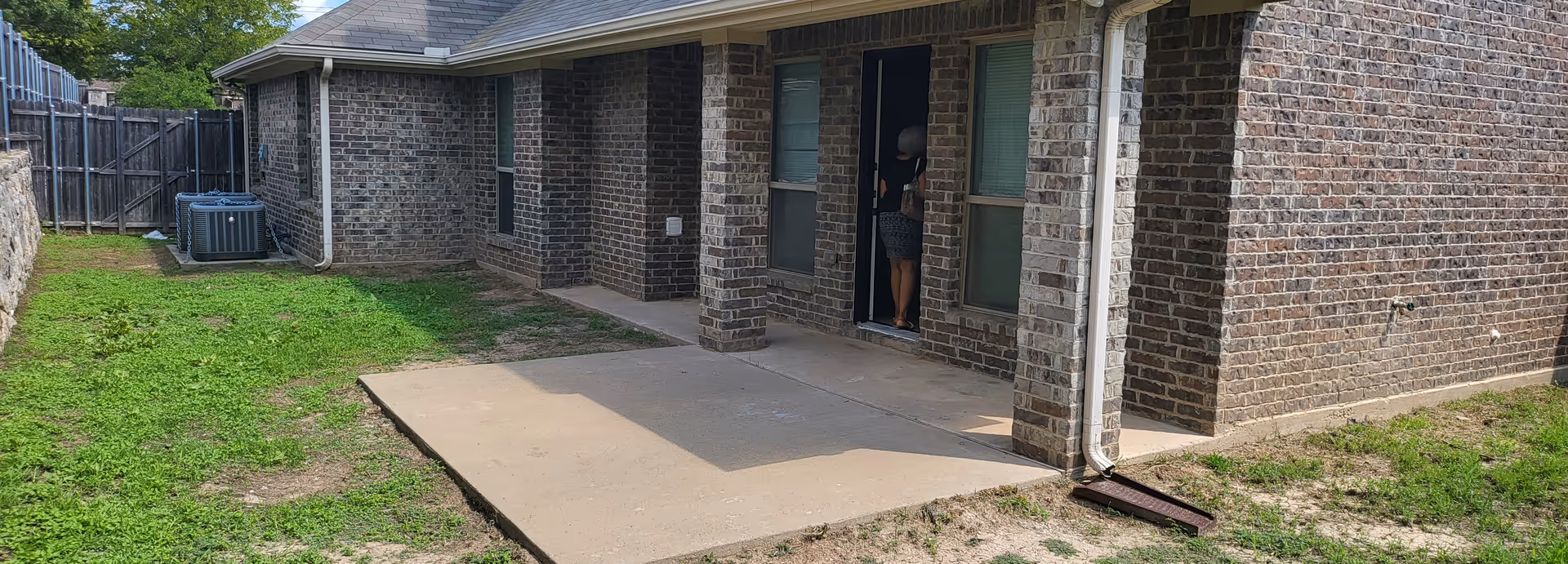 Brick senior living facility exterior with a small concrete patio and a person at the doorway.