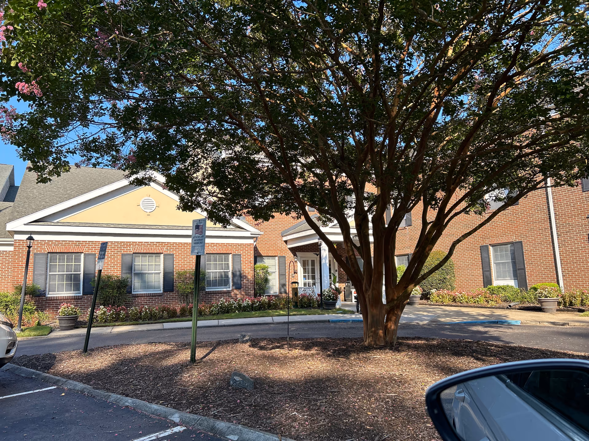 Brick Commonwealth Senior Living at King's Grant House entrance framed by a large tree.