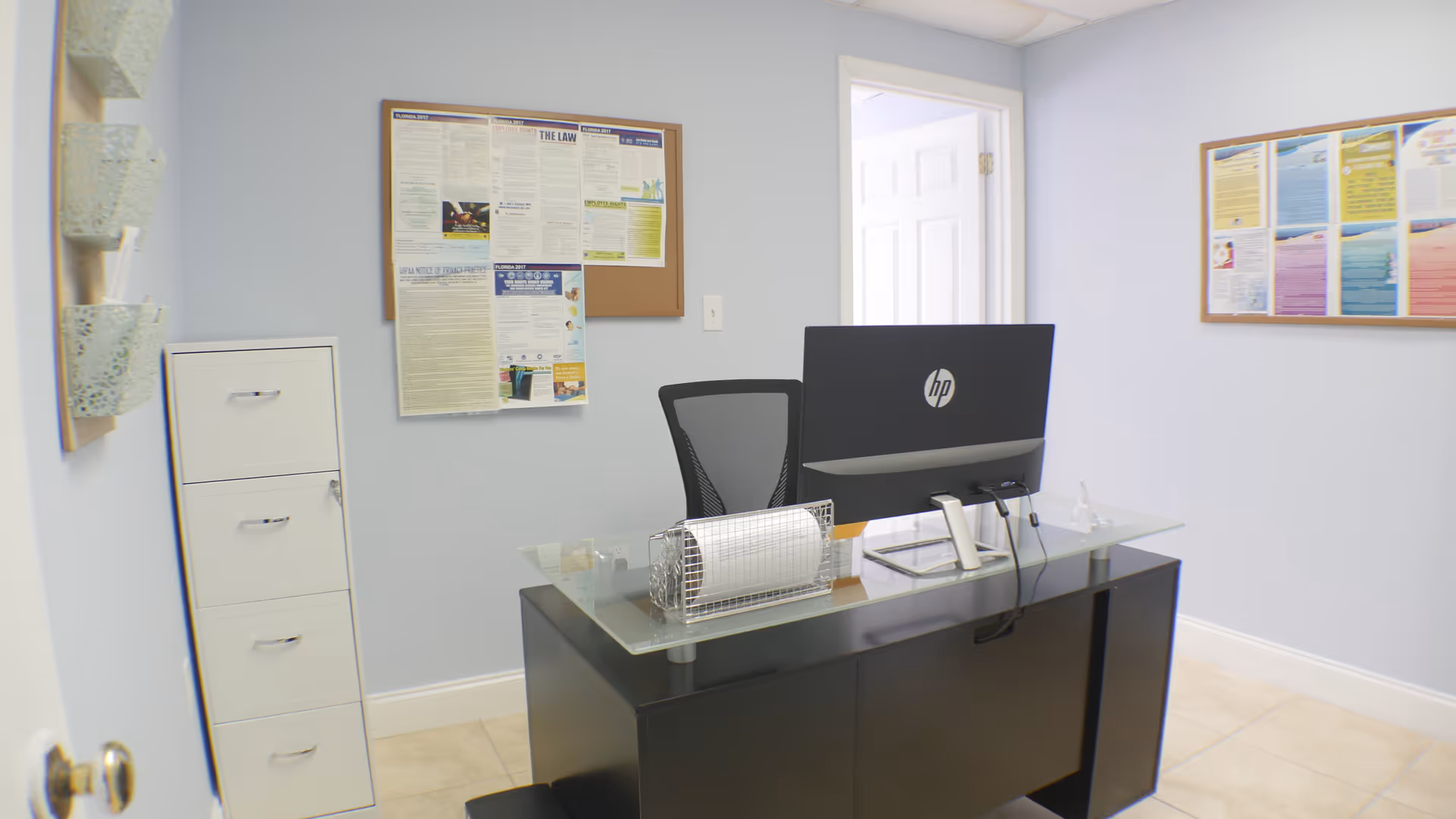Reception desk with computer, chair, and bulletin boards in a pastel-colored office.