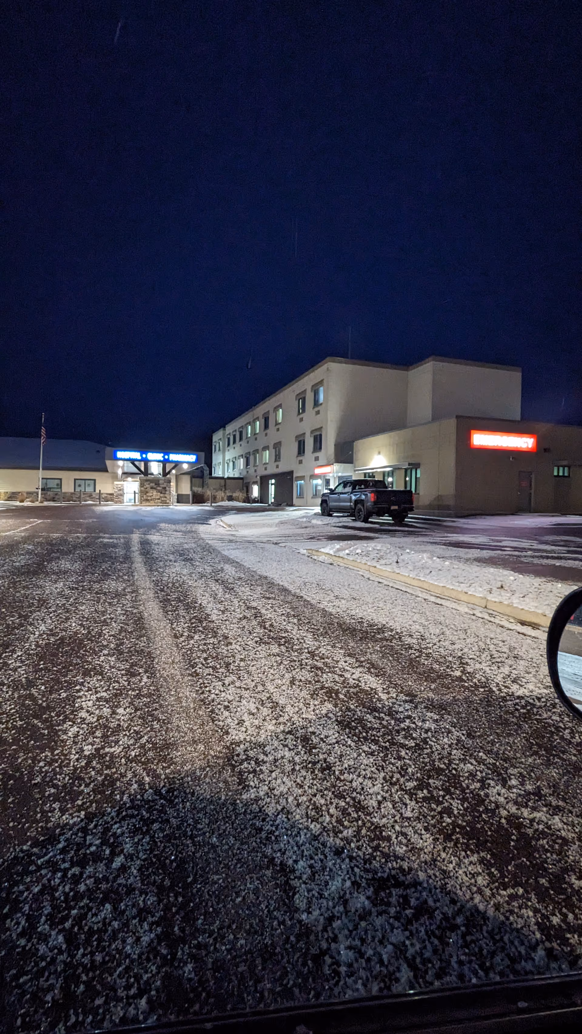 Nighttime exterior of a medical center with lit entrance and snow-covered parking lot.