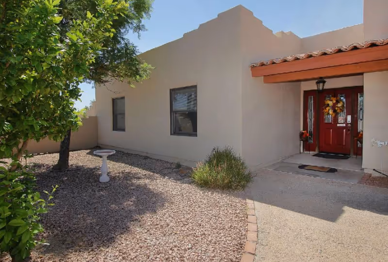 Exterior view of a beige senior living building with a red front door and desert landscaping.