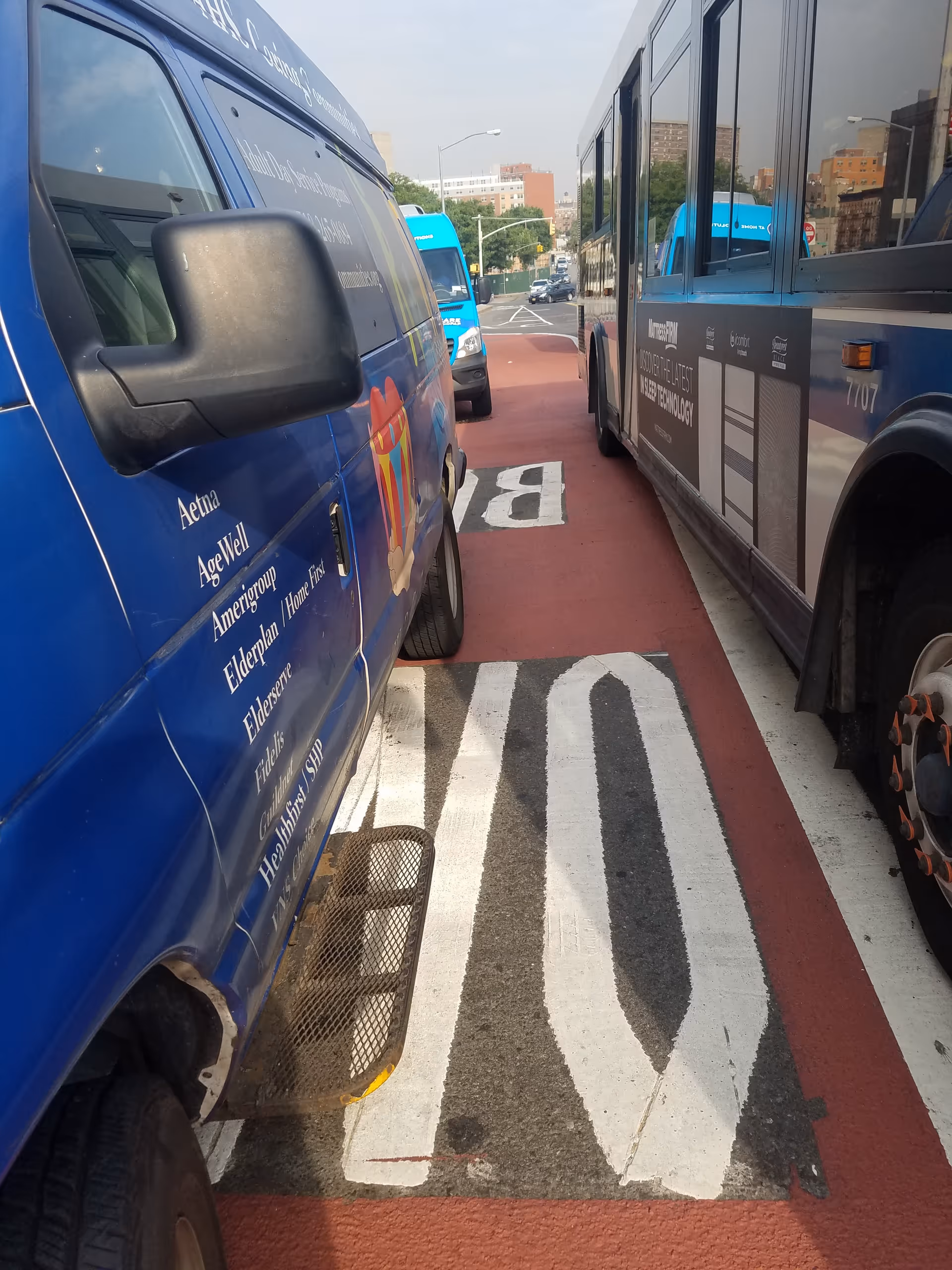 Blue branded vans parked along a city street beside a bus.