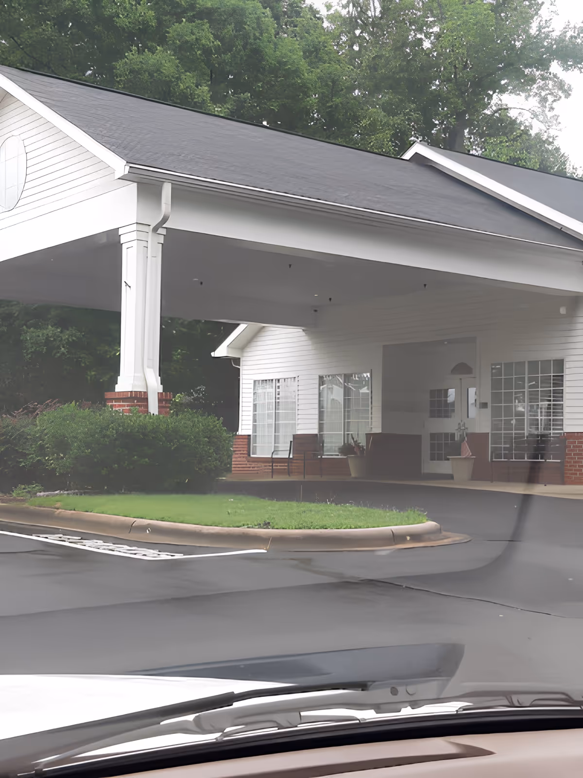 Covered entrance/portico of a white building with brick accents, seating, and landscaping seen from a parked vehicle.