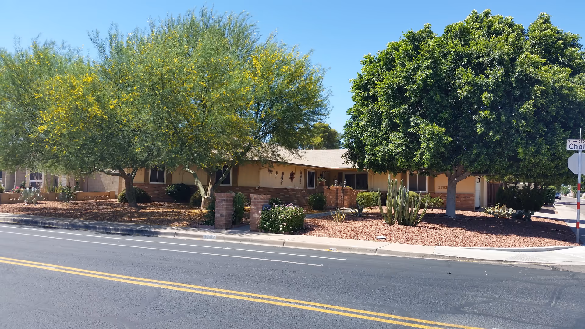 Exterior view of a single-story assisted living home with trees and desert landscaping.