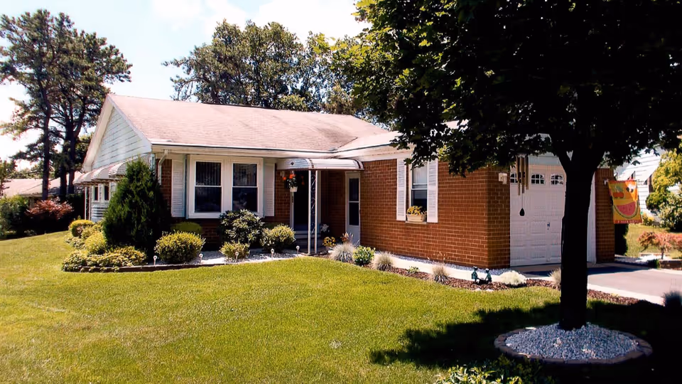 Single-story brick ranch house with a manicured front lawn, trees, and an attached garage.