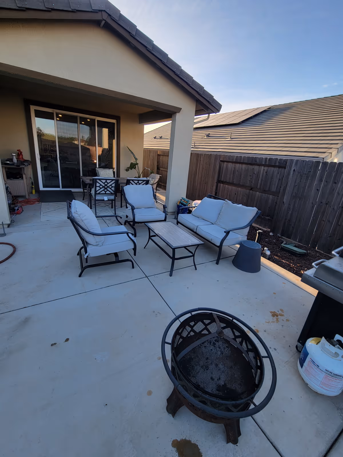 Outdoor patio with white-cushioned seating, a fire pit, grill, and sliding glass door.