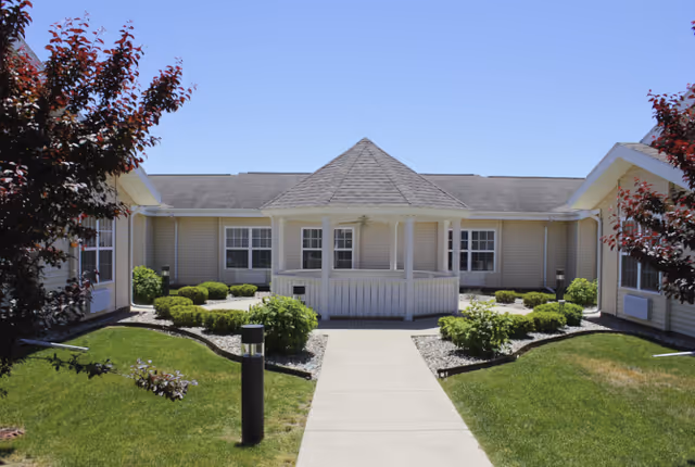 Front courtyard with a central gazebo and walkway flanked by single-story beige buildings and landscaping.