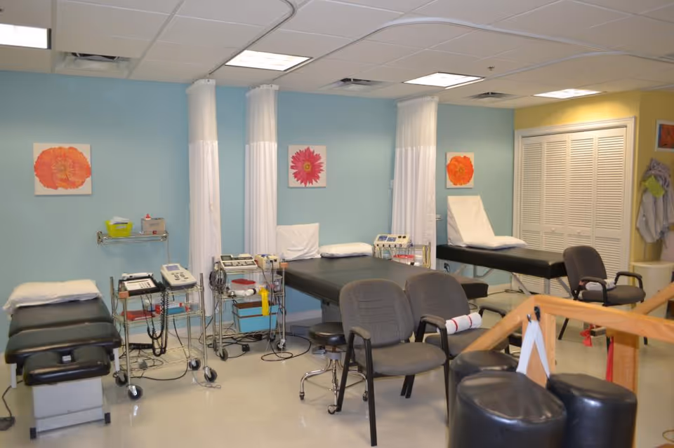 A clinical treatment room with multiple beds, curtains, and medical equipment on carts.