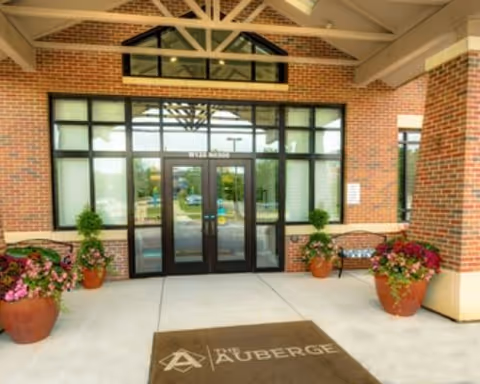 Brick-front entrance with glass doors, potted plants, and a welcome mat.