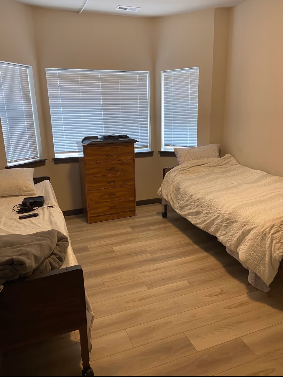 Two single beds with white bedding in a small bedroom, dresser between windows.