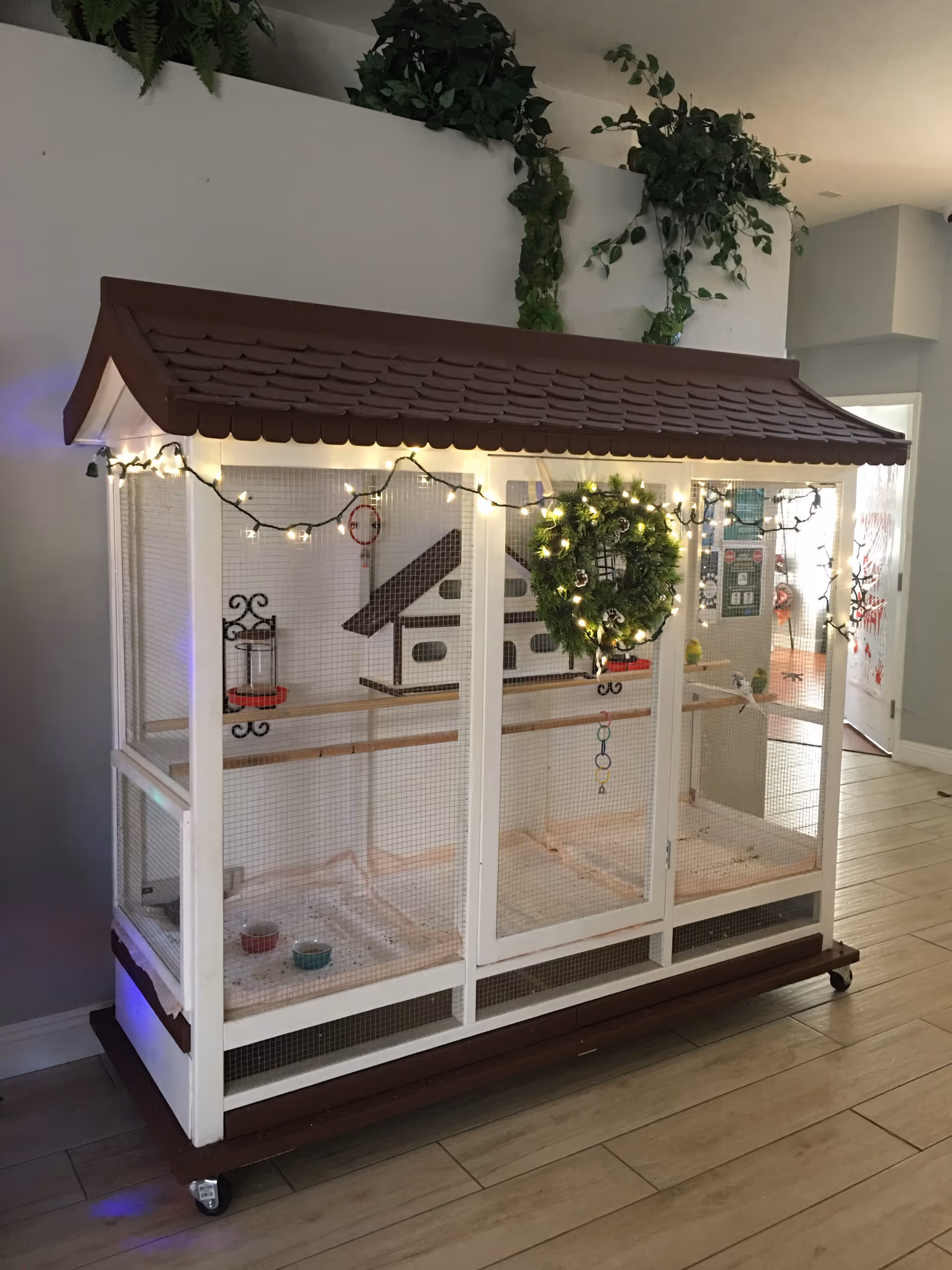 A large white wooden birdcage on wheels with a brown roof and string lights.