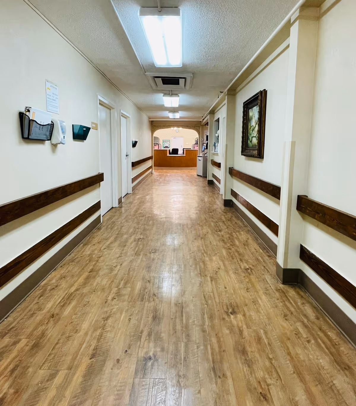 Long hallway in a senior living facility with wood railings and a distant reception desk.