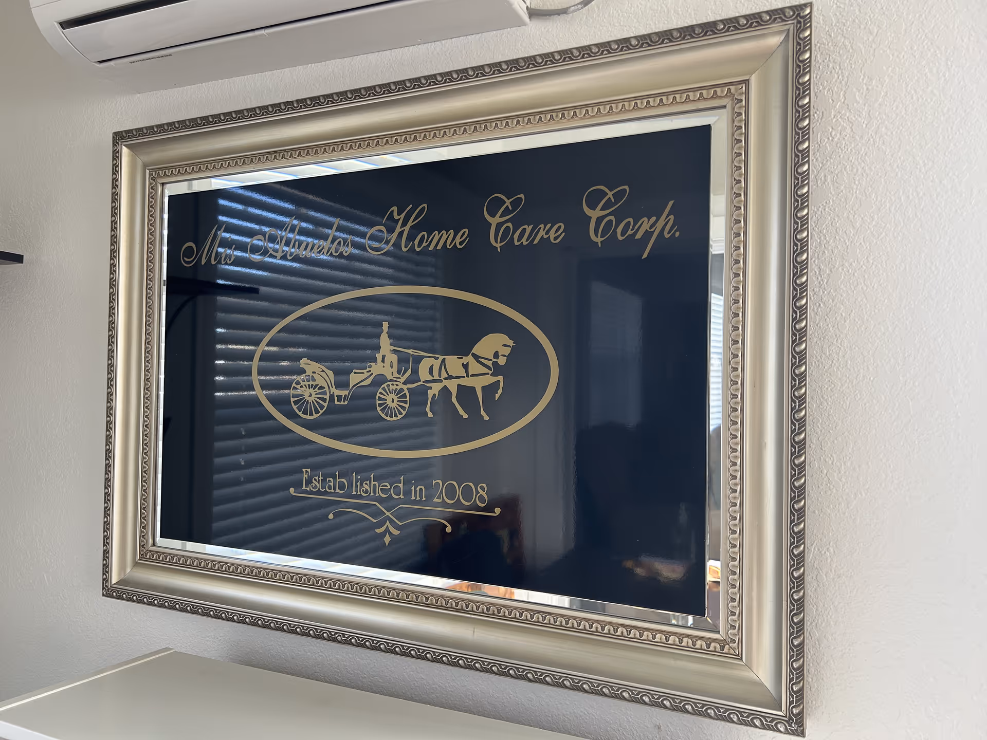 Framed Mis Abuelos Home Care Corp sign with horse-drawn carriage logo on an interior wall