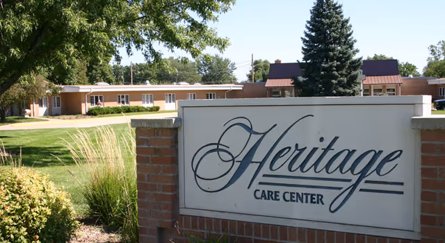 Front view of Heritage Care Center sign with brick wall and single-story building.